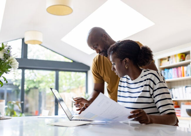 young-couple-looks-at-paperwork-and-a-laptop-in-a-sunny-dining-area