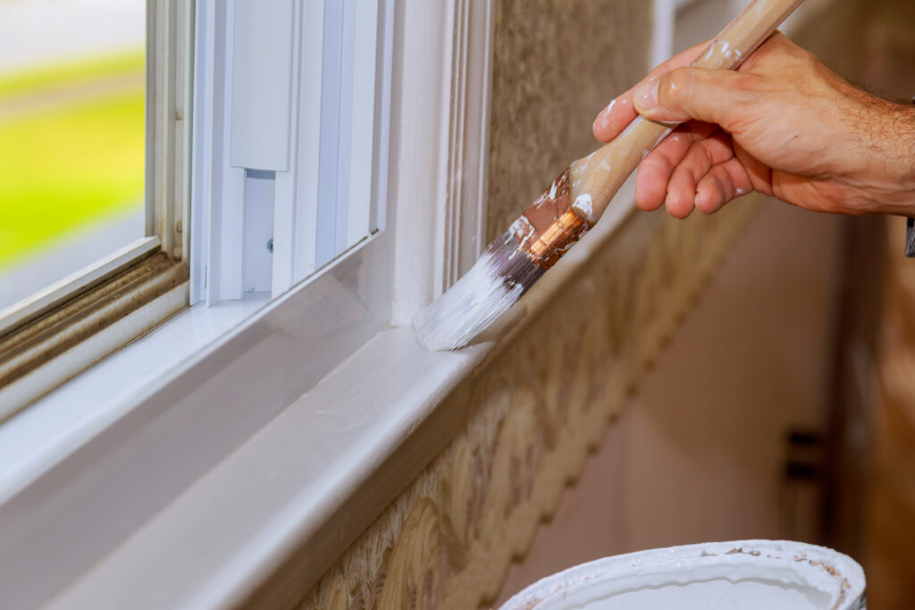 Picture of a paintbrush painting a window ledge white